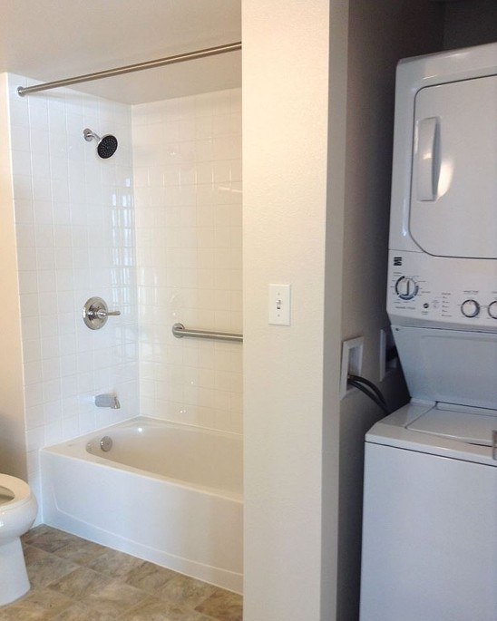 A white bathroom with a tub, toilet, and washing machine.